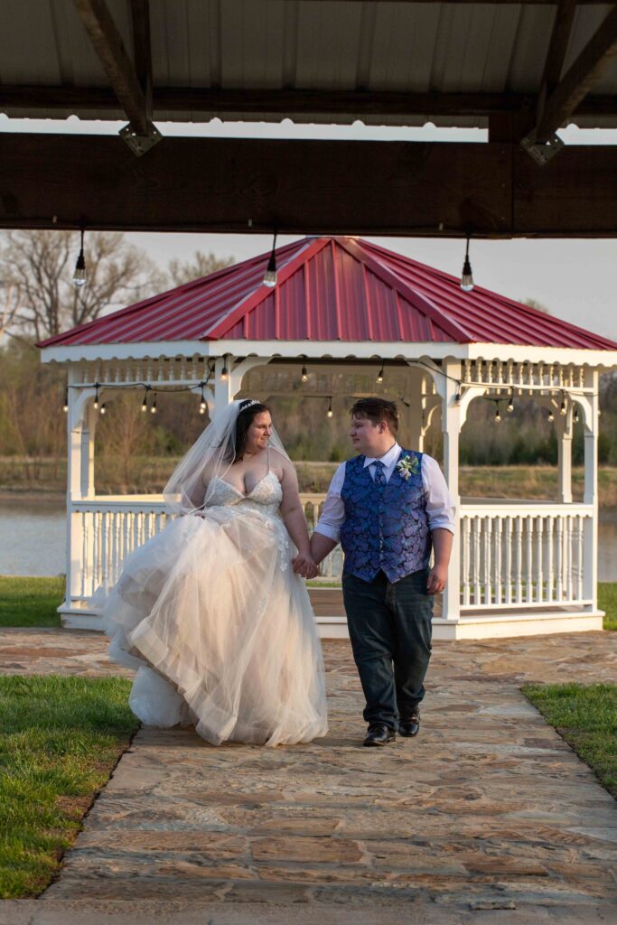 bride and groom walking with gazebo in background at lakeside wedding venue in hutchinson ks