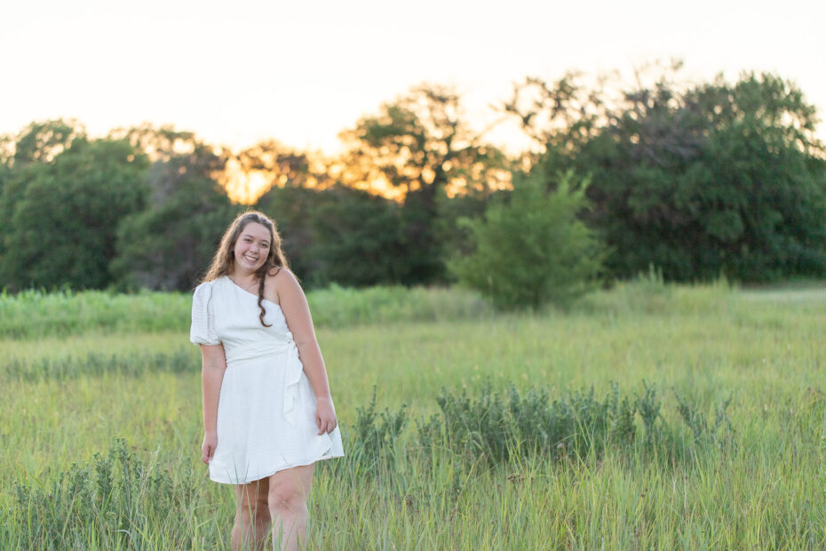 high school senior girl wearing white dress in field of tall grasses